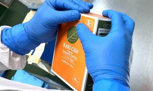 青い手袋のスタッフが、柿茶の箱を手に取って仕上げている様子
