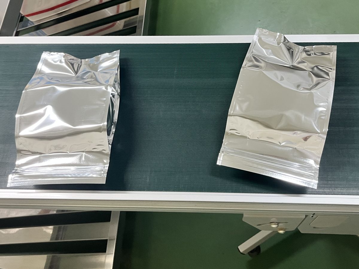 ベルトコンベアの上に置かれた、銀色のアルミ蒸着袋に入った柿茶
